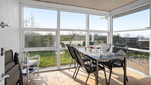 A spacious patio with a dining table and chairs, large windows offering a view of the outdoors, and a wooden ceiling. - 3 bedroom nice home in Middelfart (Middelfart)