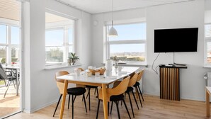 A modern dining area with a white table, black and wooden chairs, a white pendant light, and a TV mounted on the wall. - 3 bedroom nice home in Middelfart (Middelfart)