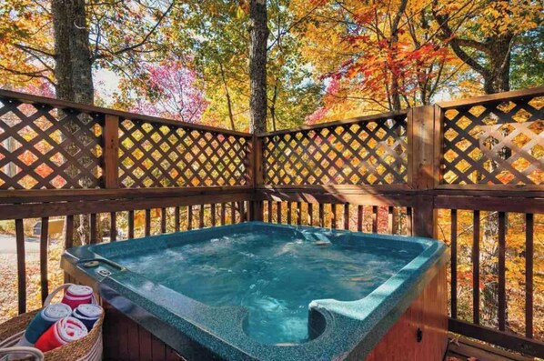 A hot tub on a wooden deck with a lattice railing, surrounded by autumn foliage. - Lovely Cabin near GSMNP & Attractions (Gatlinburg)