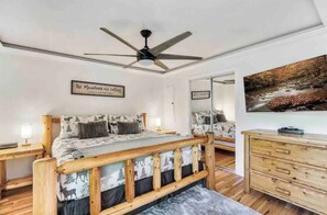 A bedroom with a wooden bed frame, a ceiling fan, a bedside table with a lamp, a dresser, and a large mirror. - Lovely Cabin near GSMNP & Attractions (Gatlinburg)