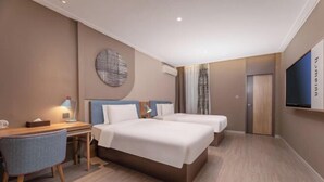 Ein Hotelzimmer mit zwei Betten, einem Schreibtisch, einem Sessel, einem Fernseher und einem Wandbild.