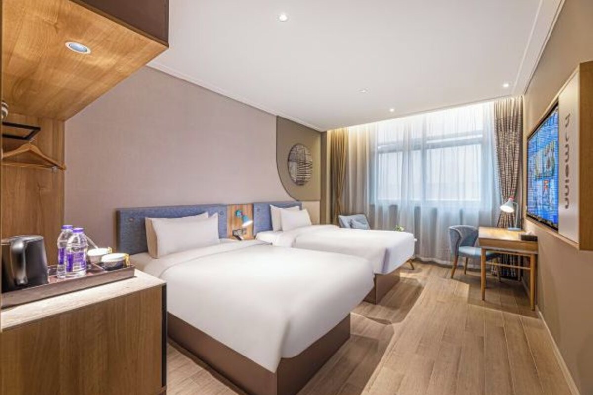 A hotel room with two beds, a desk, a chair, a TV, and a window with curtains.