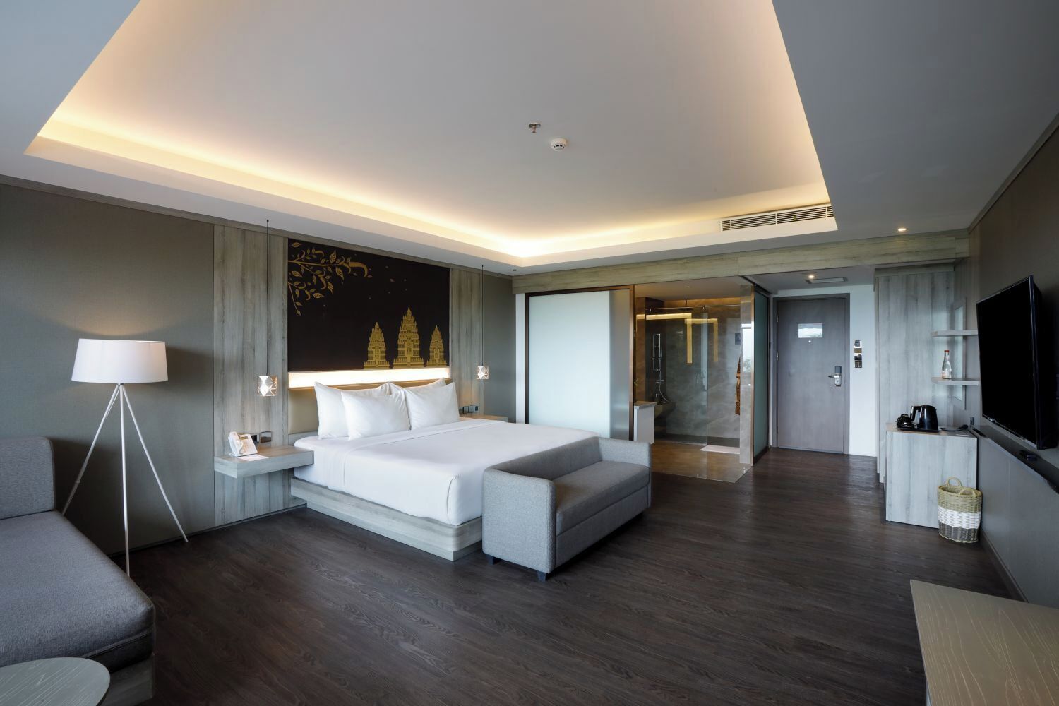 A modern hotel room with a large bed, bedside tables, a floor lamp, a TV, and a glass shower enclosure.