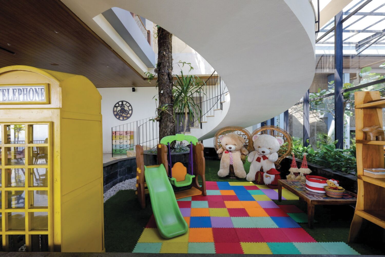 A children's play area with a slide, two large teddy bears, and a colorful play mat.