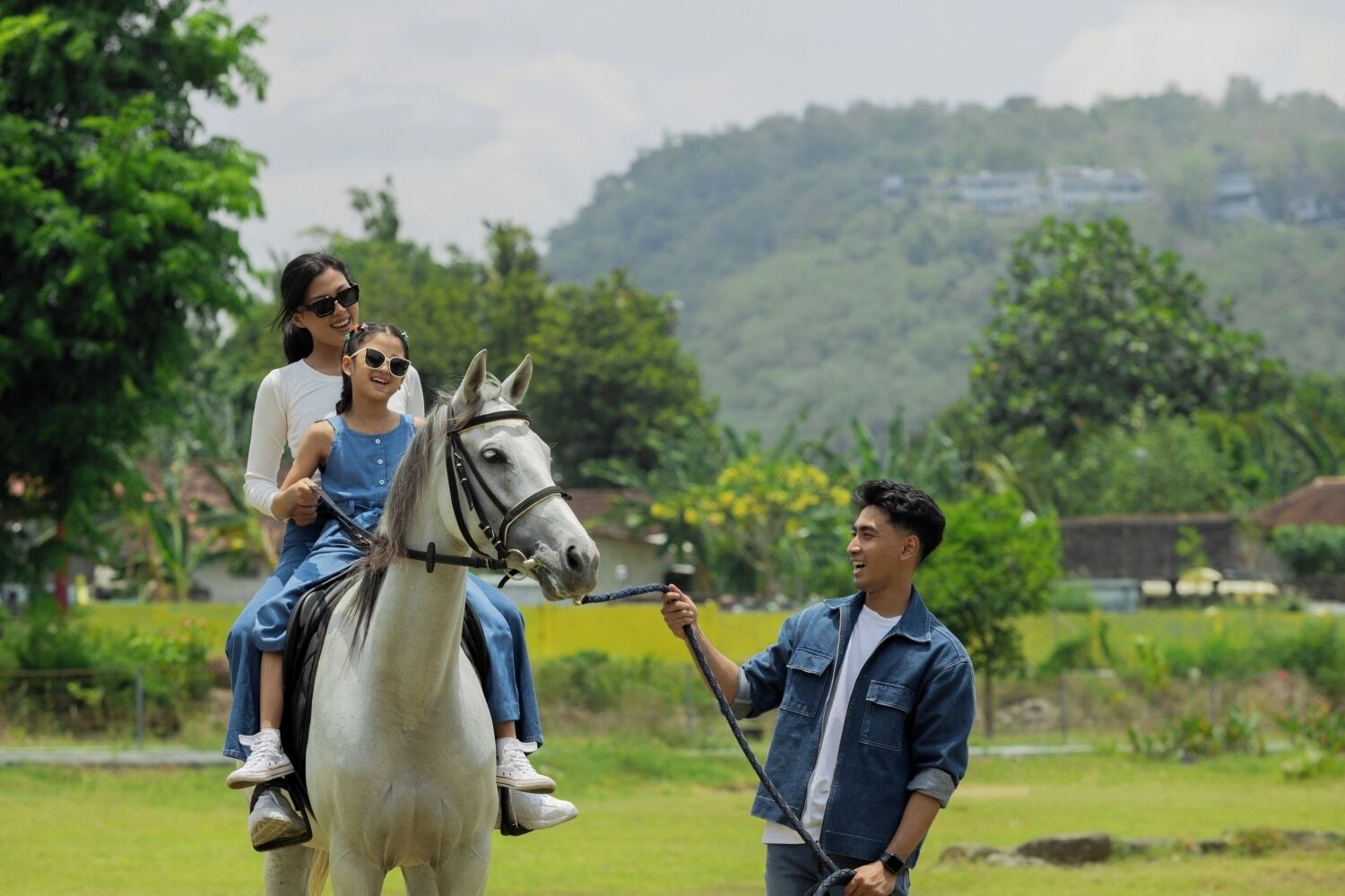 A person leading a horse with two children riding it in a rural setting.
