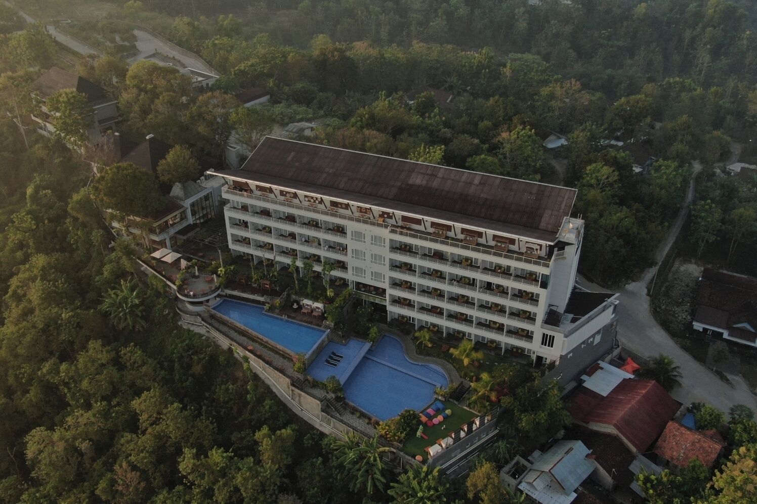 A multi-story hotel with a swimming pool and lush surrounding greenery.