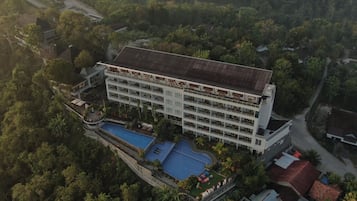 A multi-story hotel with a swimming pool and lush surrounding greenery.