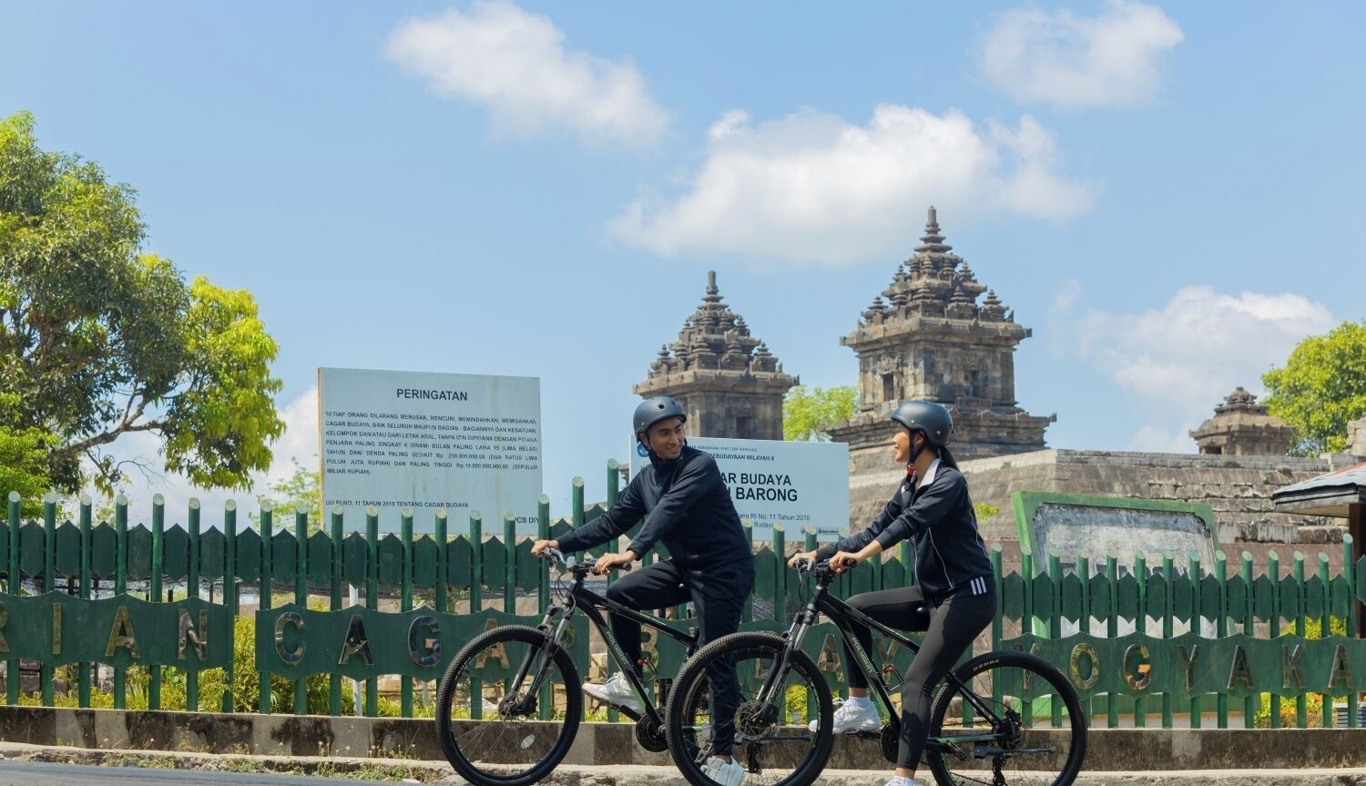 Two people riding bicycles on a bridge with a historical structure in the background.