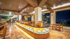 Un moderno vestíbulo de hotel con barra de buffet central, zona de estar y vistas nocturnas de la ciudad.