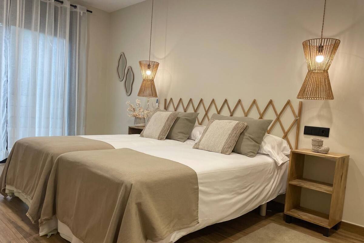 Una cama doble con dos mesitas de noche, cabecera con diseño en zigzag y dos lámparas colgantes.