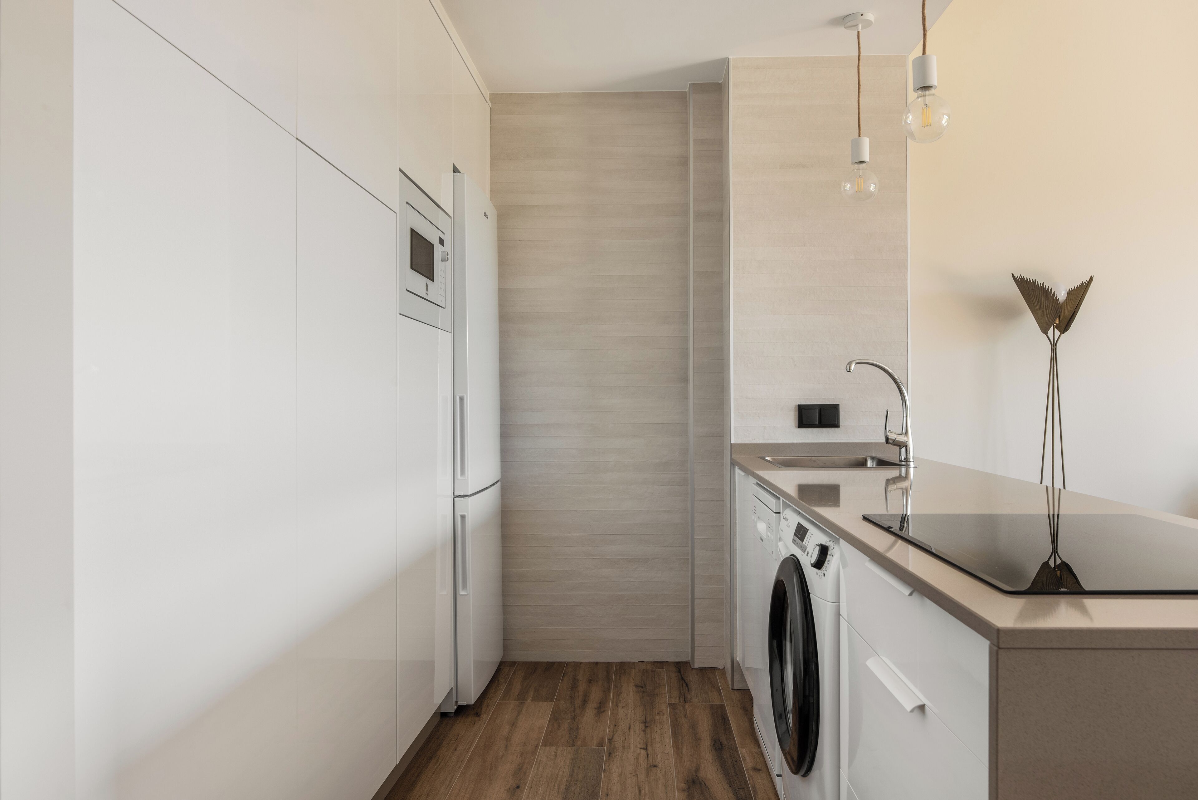 A modern kitchen with white cabinetry, a built-in oven, a washing machine, and a countertop with a sink.