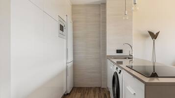 A modern kitchen with white cabinetry, a built-in oven, a washing machine, and a countertop with a sink.