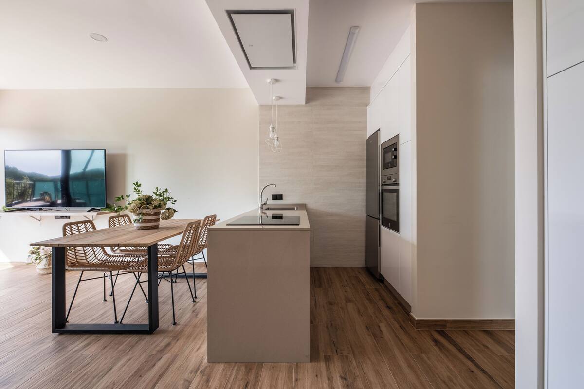 Una cocina moderna con una isla central, mesa de comedor de madera, sillas de mimbre y un televisor integrado.