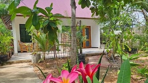 A house with a red roof, surrounded by lush greenery and a flowering plant in the foreground. - Z-VILLAGE LODGE (Jambiani)