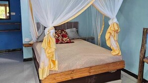 A bed with a wooden frame and a canopy, a small wooden table, and a blue wall. - Z-VILLAGE LODGE (Jambiani)