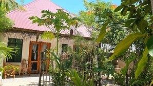 A house with a red roof, surrounded by lush greenery and a wooden fence. - Z-VILLAGE LODGE (Jambiani)
