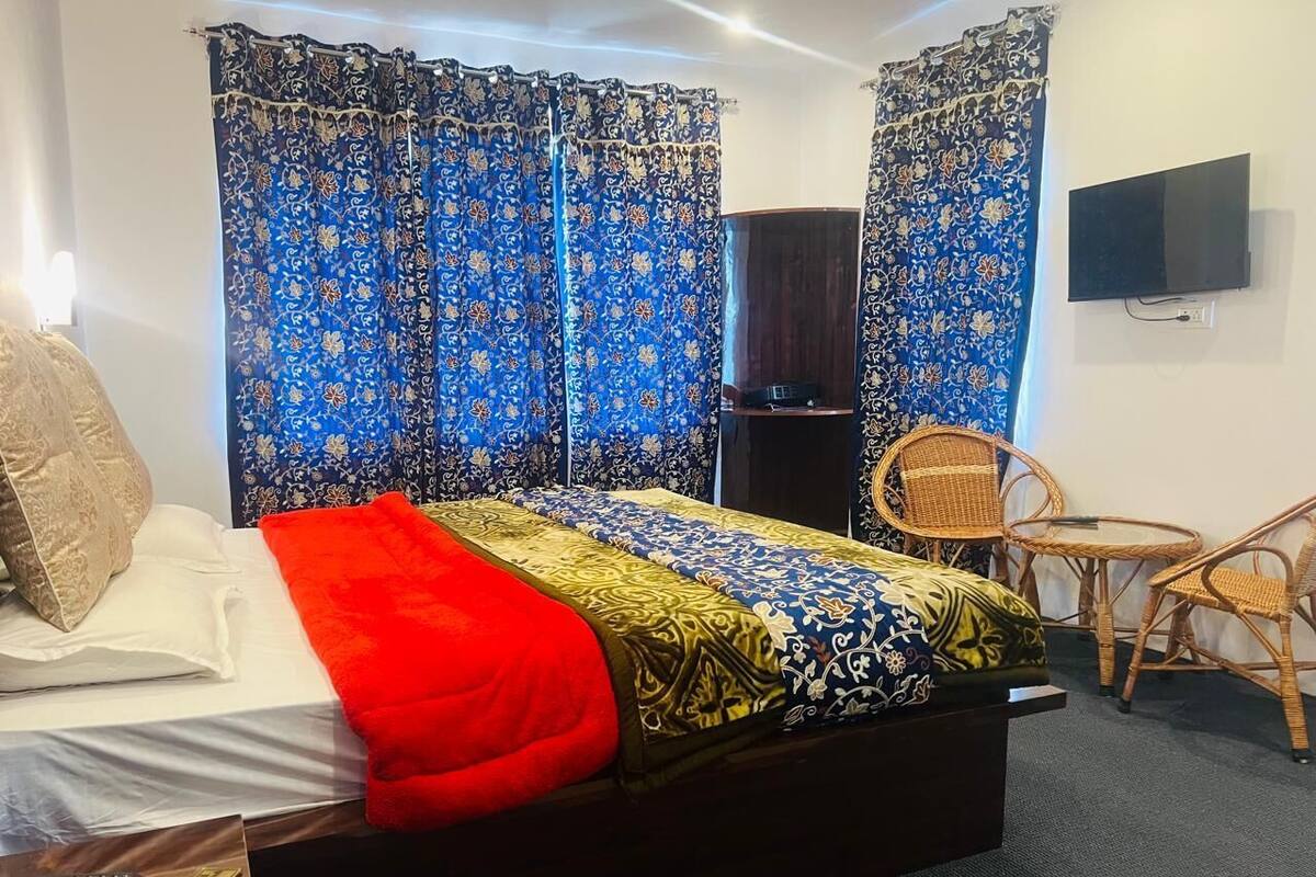 A room with a bed, a TV, a desk, and wicker furniture.