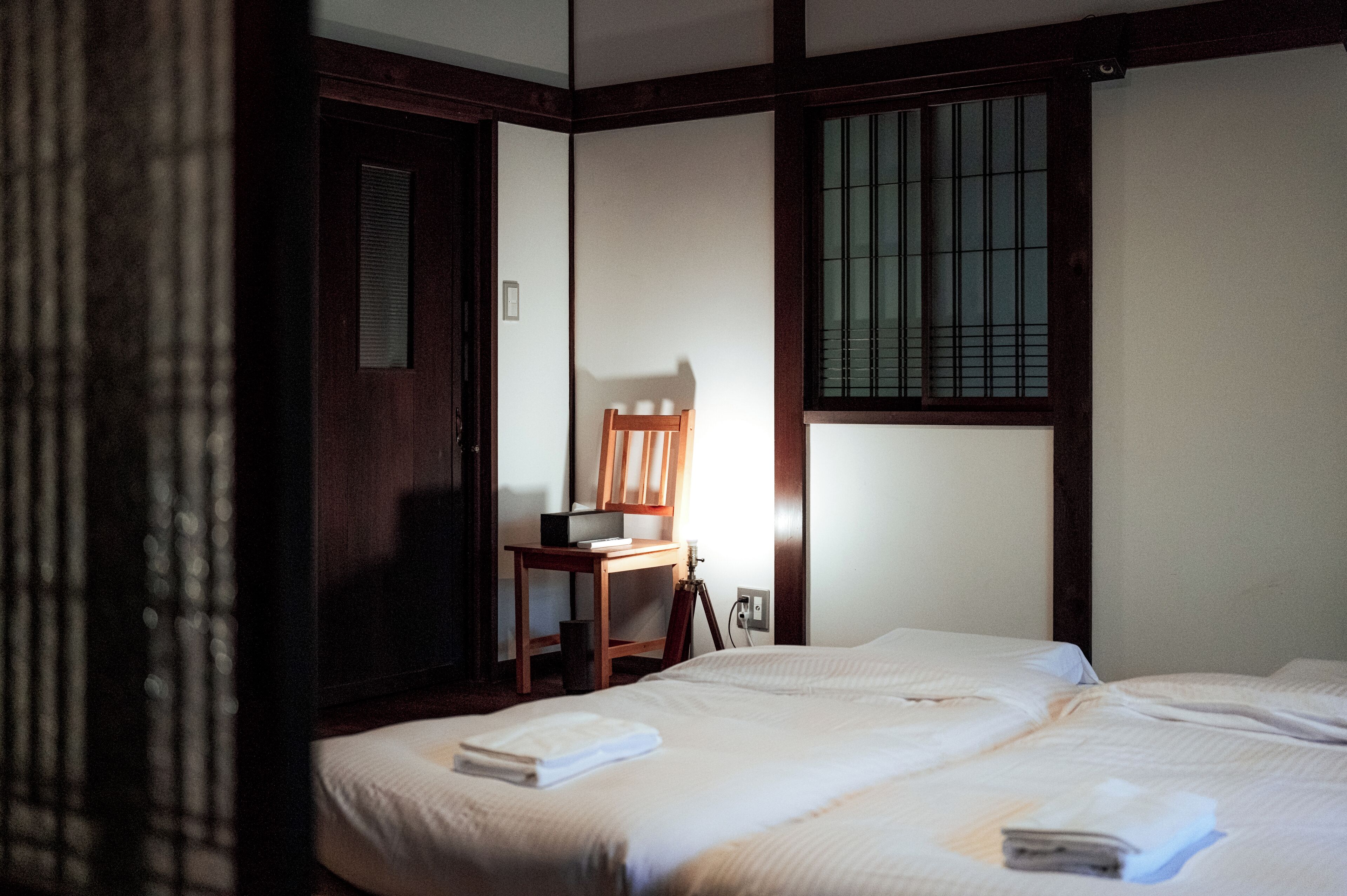 Ein Hotelzimmer mit zwei Betten, einem Holzstuhl, einem Schreibtisch und einem Fenster mit Gitterstäben.