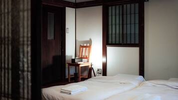 Ein Hotelzimmer mit zwei Betten, einem Holzstuhl, einem Schreibtisch und einem Fenster mit Gitterstäben.