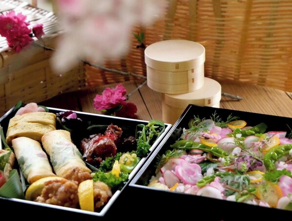 On peut voir une variété d’aliments présentés dans des plateaux noirs, notamment des petits pains, de la viande et une salade composée de radis et d’herbes aromatiques.