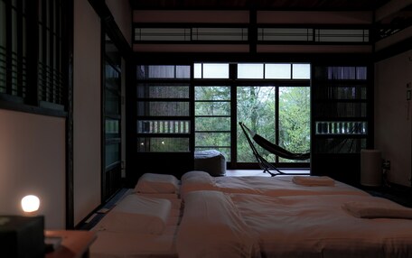 A traditional Japanese-style room with tatami flooring, a futon bed, a hammock, and large windows with a view of greenery.