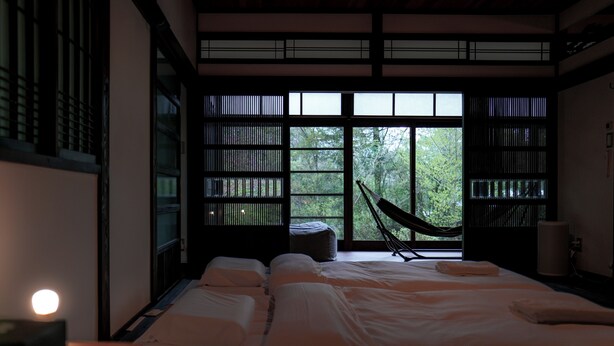 A traditional Japanese-style room with tatami flooring, a futon bed, a hammock, and large windows with a view of greenery. - EXP. Atelier (Fujinomiya)