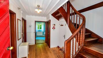 Una escalera de madera que lleva al segundo piso, un pasillo con paredes blancas y pisos de madera, y una puerta roja a la izquierda.