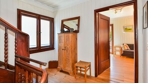 A wooden staircase, a wooden cabinet, a small stool, and a doorway leading to a living area with a sofa and a painting. - Holiday Home 'Kunterbunt' with Private Terrace, Shared Garden and Wi-Fi (Lindau)