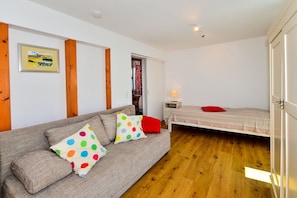 A room with a sofa, a bed, wooden flooring, a door, and a wall-mounted lamp. - Holiday Home 'Kunterbunt' with Private Terrace, Shared Garden and Wi-Fi (Lindau)