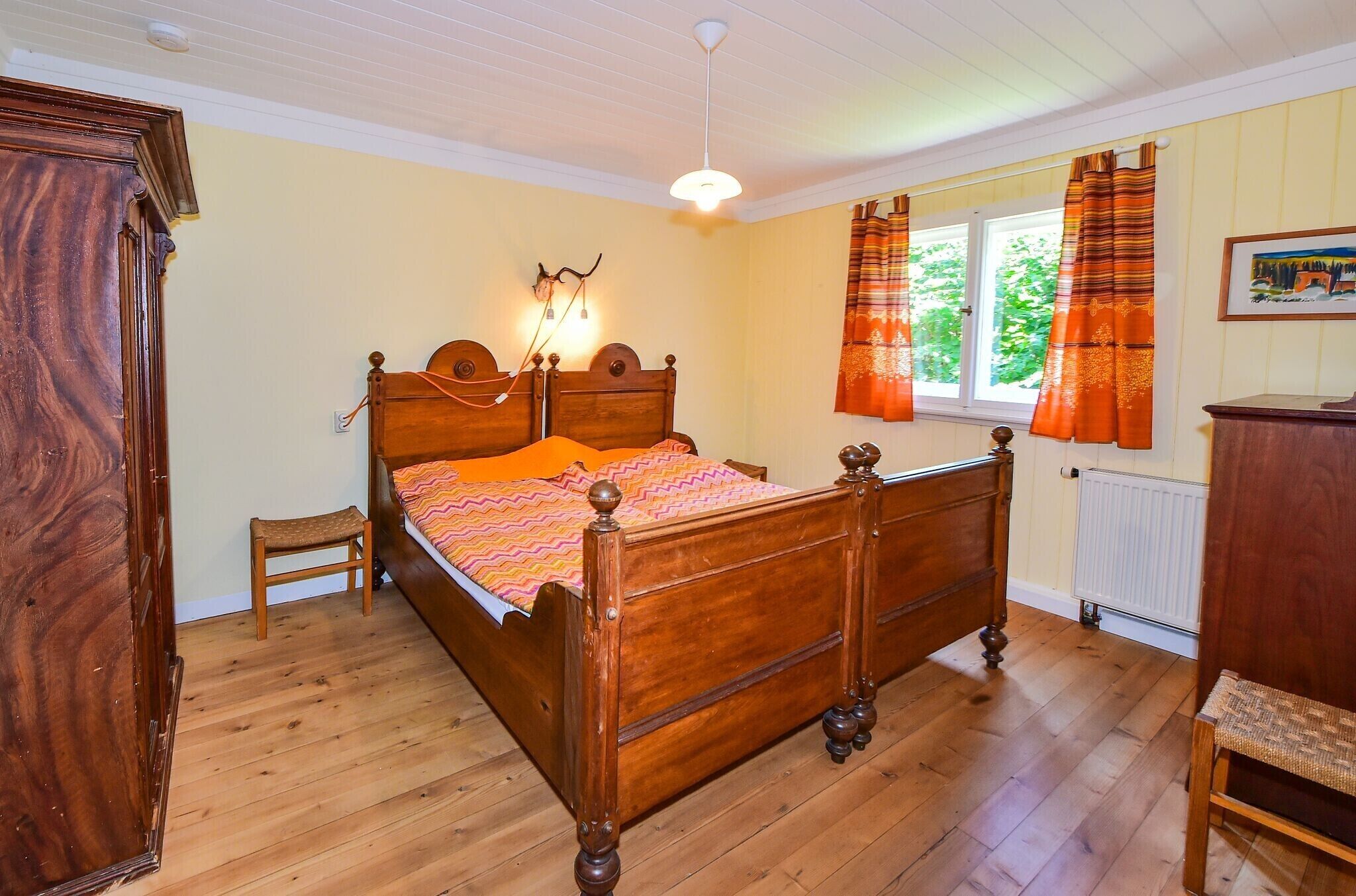 Un lit à baldaquin en bois avec une tête de lit, un petit tabouret en bois, une commode et une fenêtre avec des rideaux.