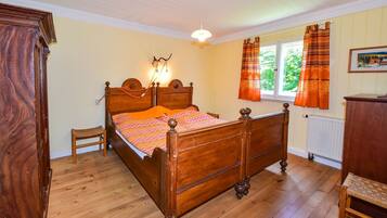 Un lit à baldaquin en bois avec une tête de lit, un petit tabouret en bois, une commode et une fenêtre avec des rideaux.