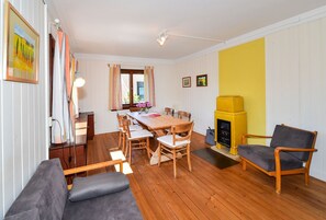 A dining area with a wooden table and chairs, a sofa, a yellow heater, and a window with curtains. - Holiday Home 'Kunterbunt' with Private Terrace, Shared Garden and Wi-Fi (Lindau)
