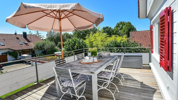 A wooden deck with a table and chairs, an umbrella, and a railing. - Holiday Home 'Kunterbunt' with Private Terrace, Shared Garden and Wi-Fi (Lindau)