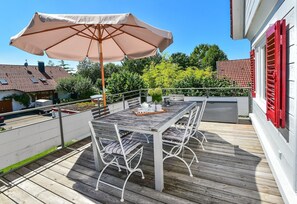 Une terrasse en bois avec une table et des chaises, un parasol et une rambarde.