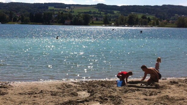 A lake with a sandy beach, a child playing, and a person in red.