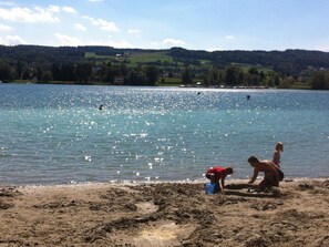 A lake with a sandy beach, a child playing, and a person in red.