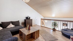 A loft-style living room with a wooden ceiling, a sofa, a coffee table, a staircase, and a balcony with a plant.