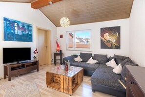 Uma sala de estar com sofá, televisão, mesa de centro de madeira e obras de arte nas paredes.
