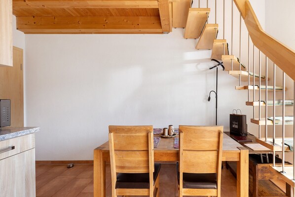 A dining area with wooden chairs and a table, a staircase with wooden railings, and a kitchen area with a microwave.