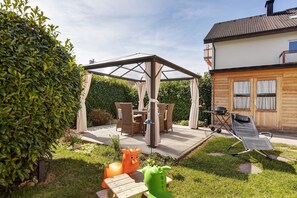 Un portico coperto con tavolo e sedie, un barbecue e una poltrona a dondolo.