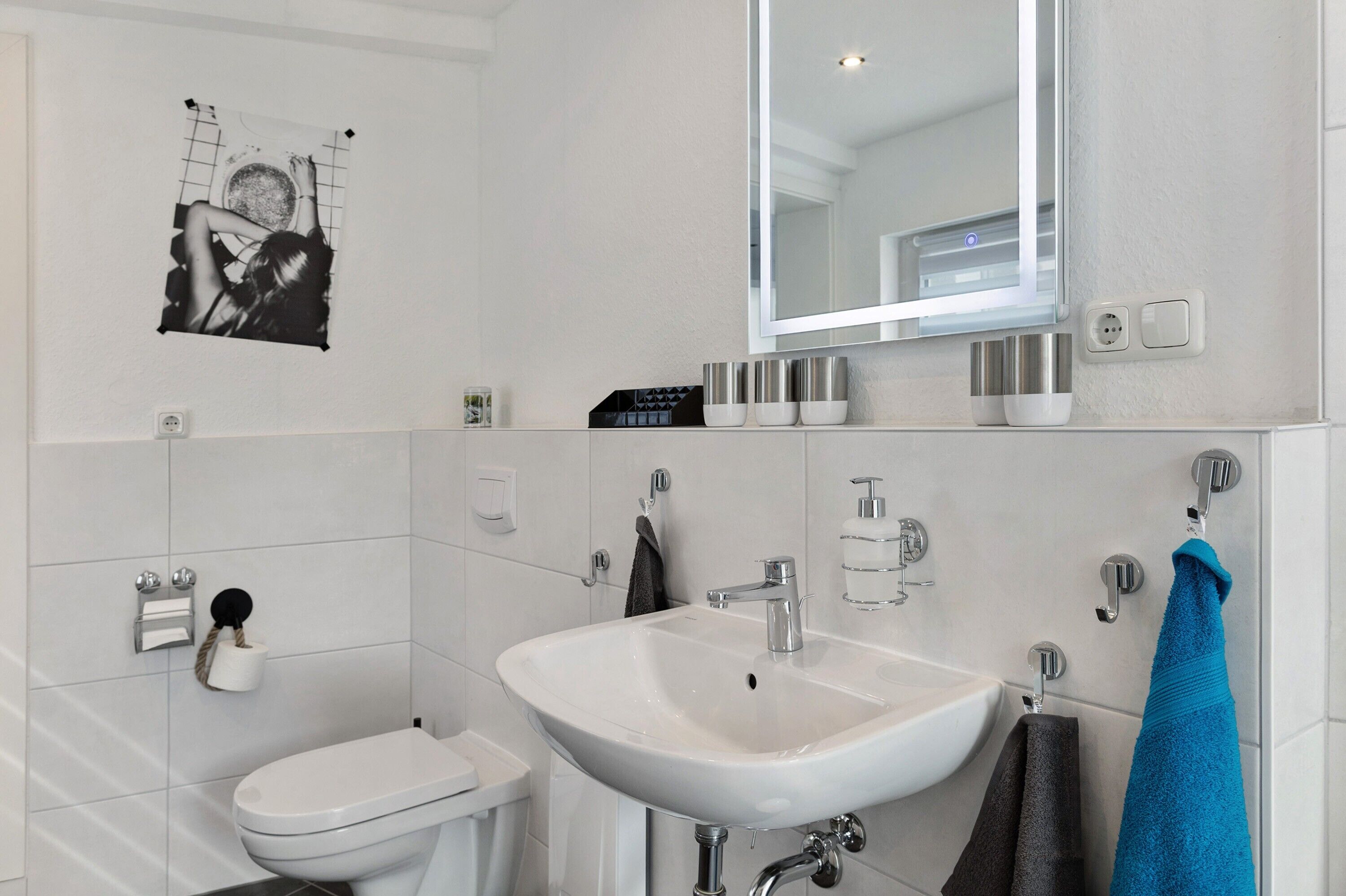 A modern bathroom with a white sink, a toilet, a mirror, and a towel rack.