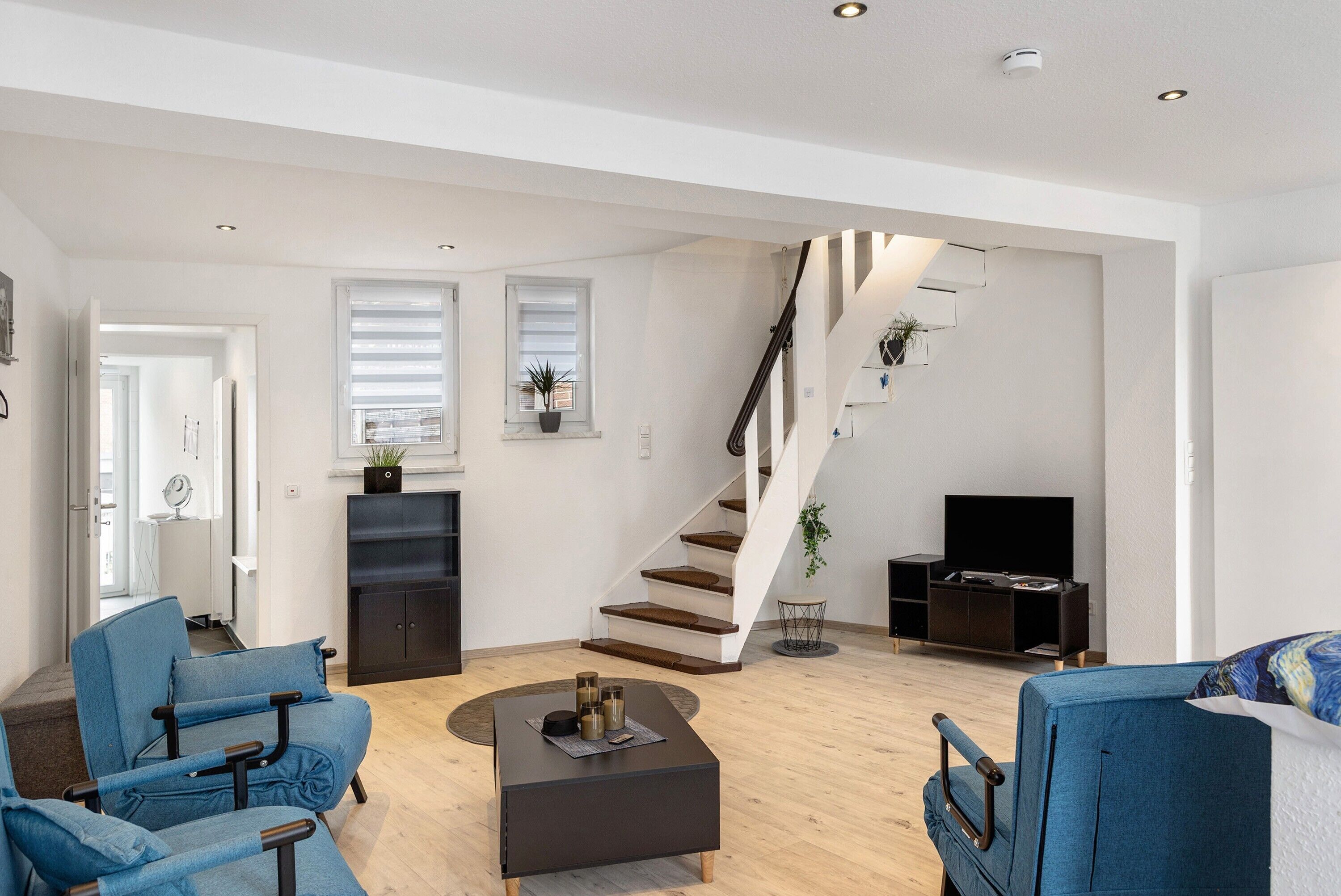 Ein geräumiges Wohnzimmer mit Treppe, Flachbildfernseher und einer Sitzecke mit blauen Sesseln.
