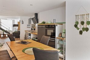A modern kitchen with a wooden dining table, chairs, and a coffee machine.