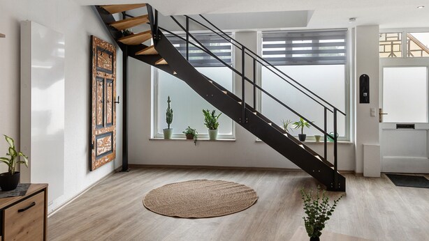Een modern interieur met een houten vloer, een zwart spiraaltrap en potplanten bij de ramen.