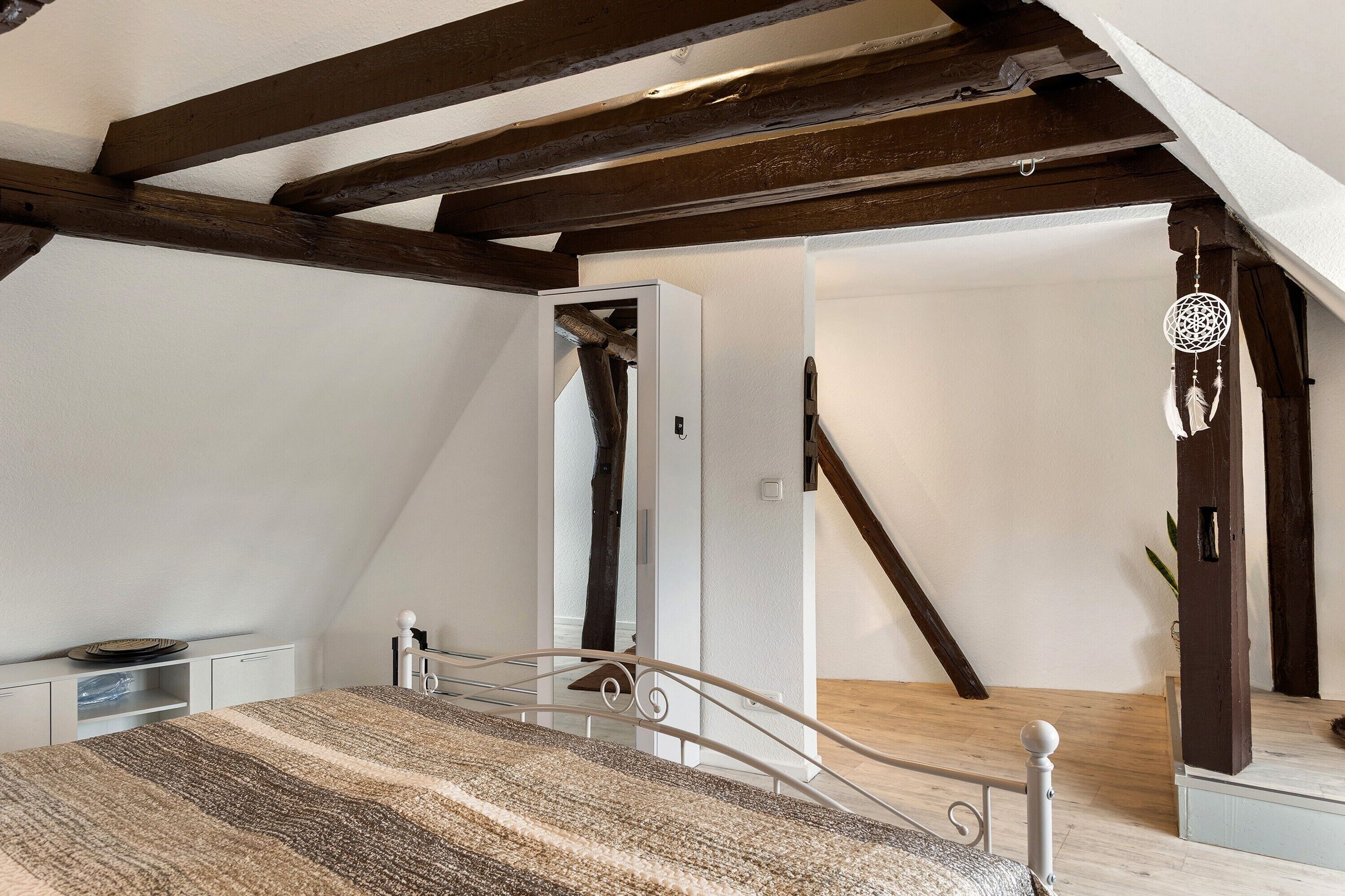 Une chambre à coucher avec un lit, un plafond en bois, un mur blanc et un escalier.