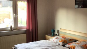 Une chambre à coucher avec un lit en bois, une fenêtre avec des rideaux, un radiateur et une lampe fixée au mur.