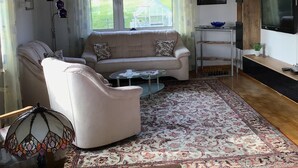 Un salon avec un canapé, un fauteuil, une table basse, un téléviseur et une horloge au mur.
