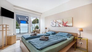 A bedroom with a large bed, a TV, a bedside table, and a view of the outside. - Apartment 'Schilfbrise' with Balcony and Wi-Fi (Wunstorf)