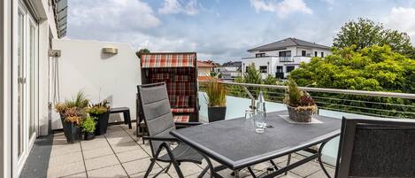 A balcony with a table and chairs, potted plants, and a plaid tablecloth.