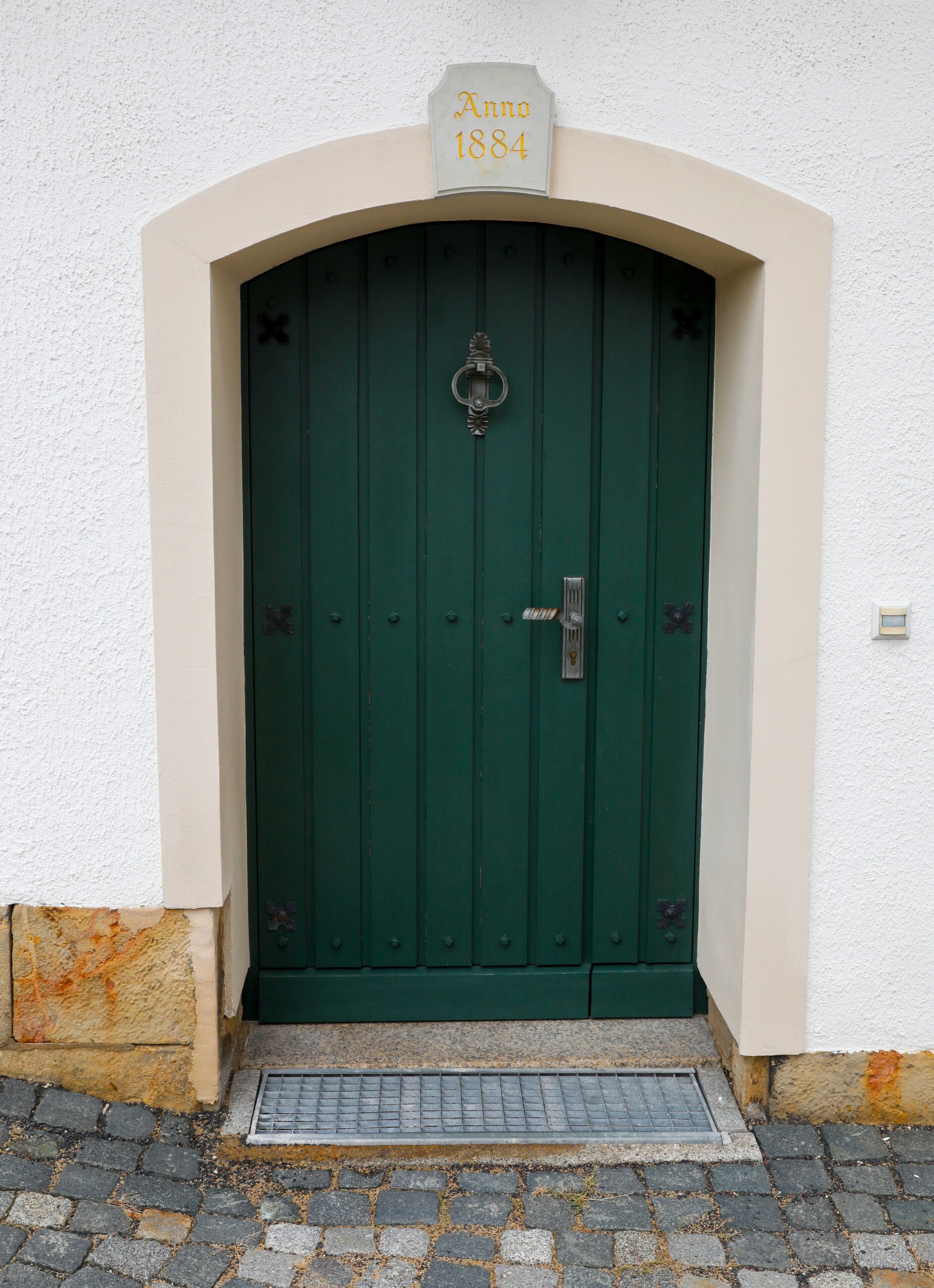 A green door with a sign above it reading 'Anno 1884.'